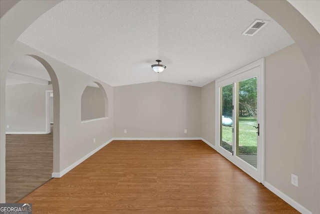 spare room featuring lofted ceiling, wood-type flooring, and a textured ceiling