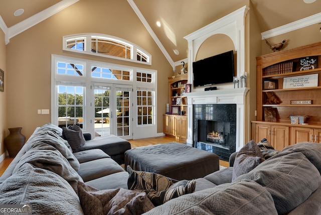 living room featuring high vaulted ceiling, a tiled fireplace, ornamental molding, french doors, and light hardwood / wood-style floors