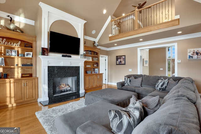 living room with a fireplace, high vaulted ceiling, crown molding, light hardwood / wood-style flooring, and ceiling fan