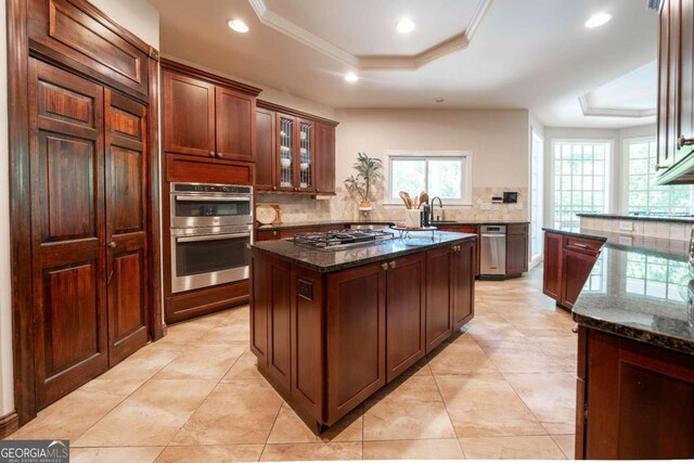 kitchen with backsplash, dark stone countertops, stainless steel appliances, and a tray ceiling