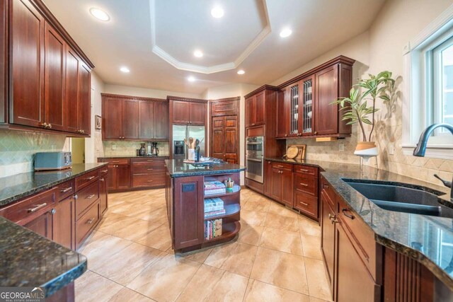 kitchen with dark stone countertops, a center island, appliances with stainless steel finishes, sink, and a raised ceiling