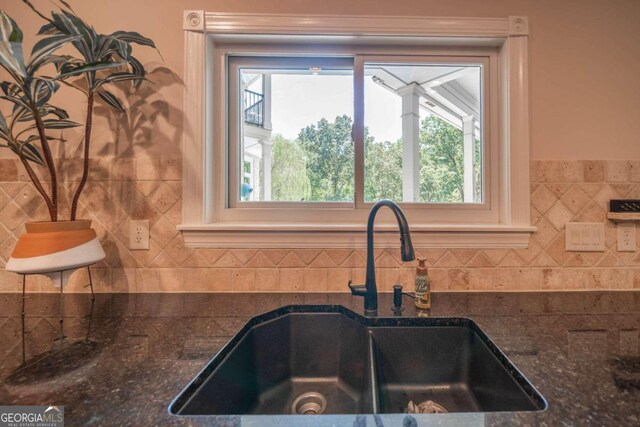 kitchen featuring a healthy amount of sunlight, sink, tile walls, and dark stone counters