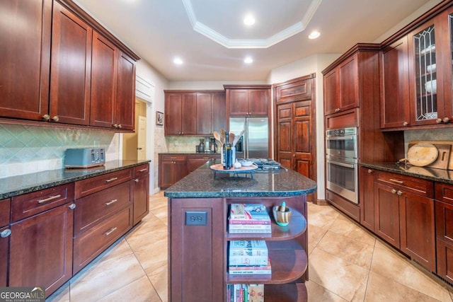 kitchen with a tray ceiling, a center island, stainless steel appliances, decorative backsplash, and dark stone counters