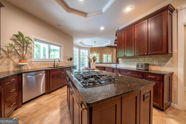 kitchen with a tray ceiling, a center island, stainless steel appliances, sink, and dark stone counters