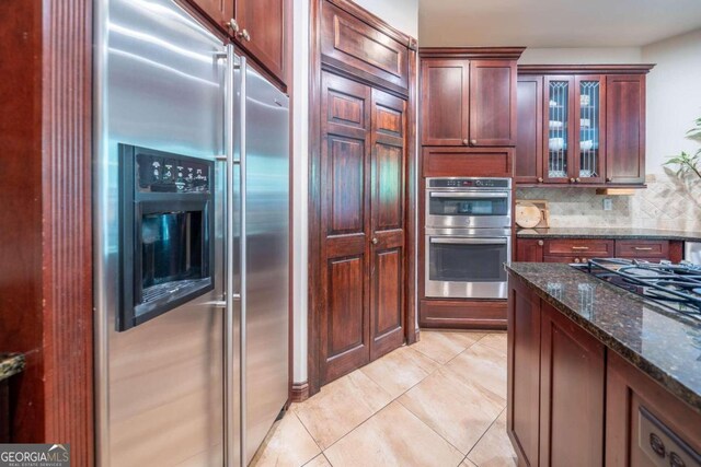 kitchen with light tile patterned floors, appliances with stainless steel finishes, dark stone countertops, and decorative backsplash