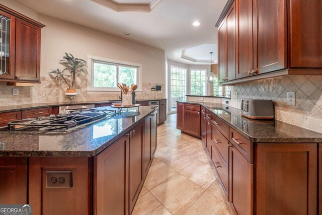 kitchen featuring stainless steel gas stovetop, decorative backsplash, a raised ceiling, and dark stone counters