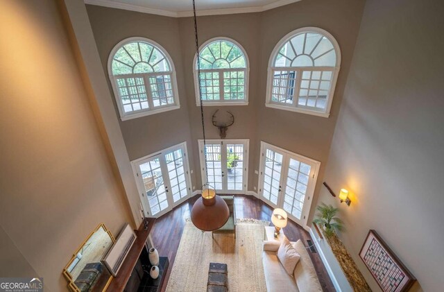 living room with a towering ceiling, ornamental molding, french doors, and hardwood / wood-style flooring