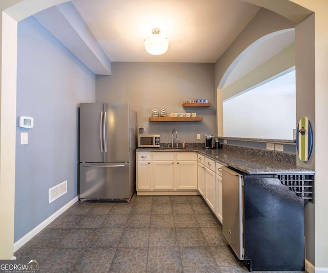 kitchen with appliances with stainless steel finishes, dark tile patterned flooring, sink, white cabinetry, and dark stone counters