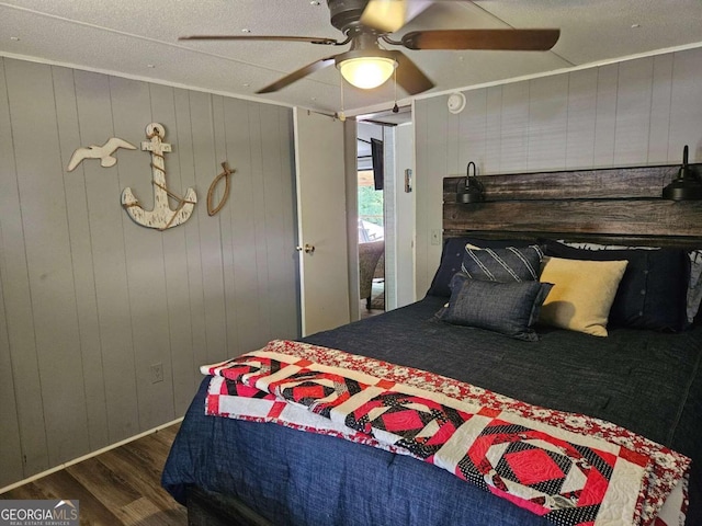 bedroom with a textured ceiling, wooden walls, ceiling fan, and dark hardwood / wood-style floors