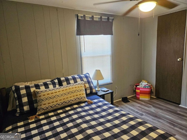 bedroom featuring hardwood / wood-style floors, ceiling fan, and wood walls