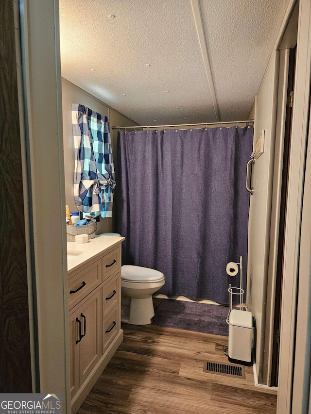 bathroom featuring toilet, walk in shower, vanity, a textured ceiling, and wood-type flooring