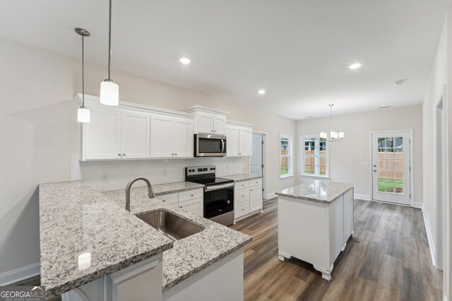 kitchen with dark hardwood / wood-style floors, decorative light fixtures, appliances with stainless steel finishes, kitchen peninsula, and sink