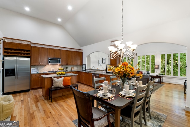 dining area with an inviting chandelier, light hardwood / wood-style flooring, sink, and high vaulted ceiling