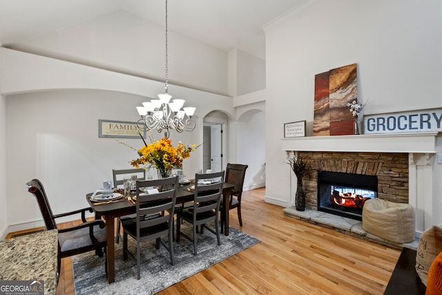 dining room with high vaulted ceiling, a stone fireplace, an inviting chandelier, hardwood / wood-style flooring, and ornamental molding