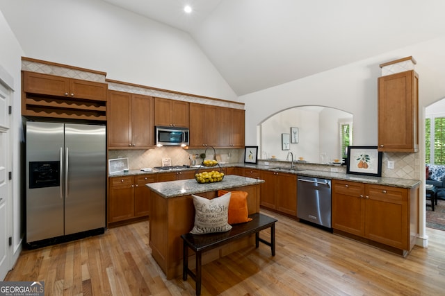 kitchen with light stone counters, sink, light hardwood / wood-style flooring, high vaulted ceiling, and stainless steel appliances