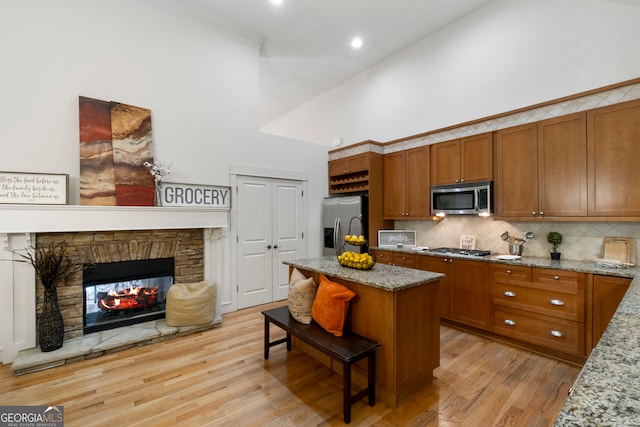 kitchen with light hardwood / wood-style flooring, stainless steel appliances, a fireplace, a high ceiling, and light stone countertops