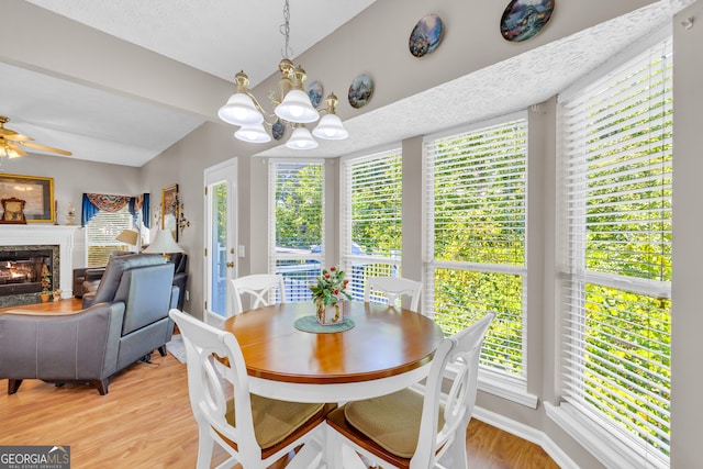 dining space featuring light wood-type flooring, ceiling fan with notable chandelier, a fireplace, and a textured ceiling