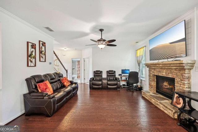 living room featuring dark wood-type flooring, ceiling fan, ornamental molding, and a stone fireplace