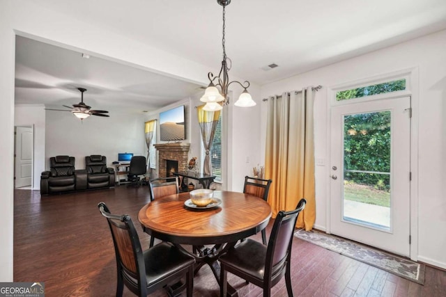 dining room with ceiling fan with notable chandelier, a fireplace, and dark hardwood / wood-style flooring