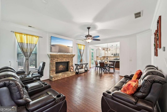 living room featuring dark wood-type flooring, ceiling fan, a fireplace, and crown molding