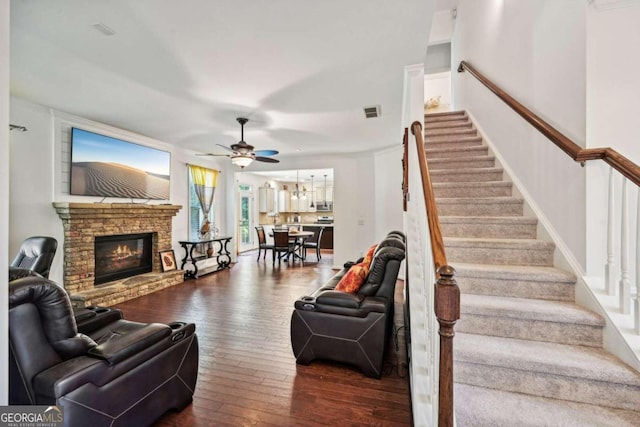 living room with ceiling fan, dark hardwood / wood-style flooring, and a stone fireplace