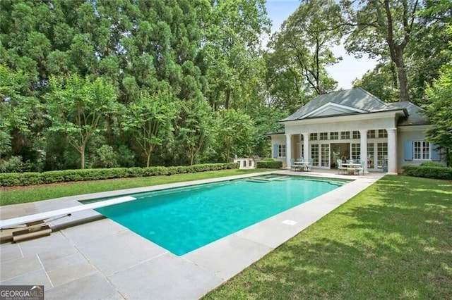 view of pool with a diving board, a lawn, and a patio area