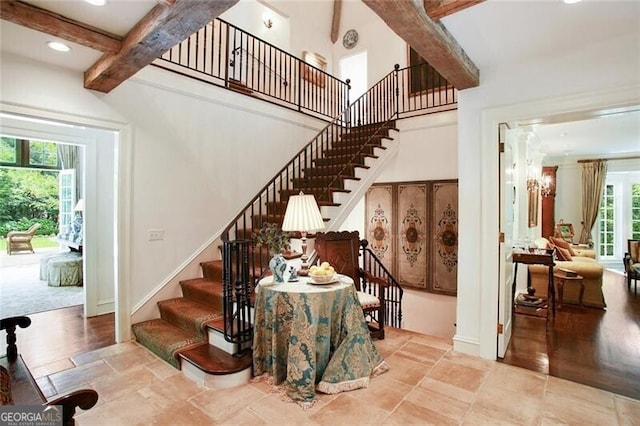 stairway featuring a wealth of natural light, beamed ceiling, hardwood / wood-style floors, and a towering ceiling