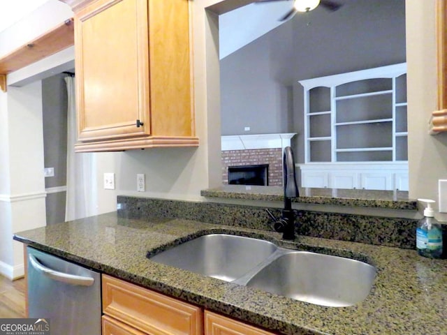 kitchen with ceiling fan, a brick fireplace, dark stone countertops, stainless steel dishwasher, and sink