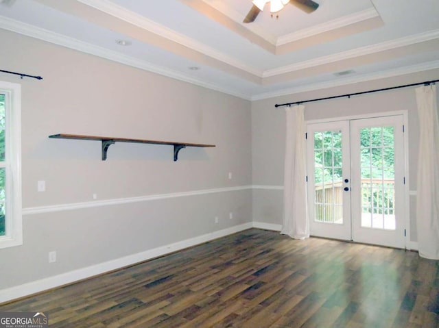 empty room featuring ceiling fan, a tray ceiling, dark wood-type flooring, ornamental molding, and french doors