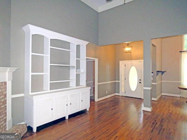 entryway with a brick fireplace, crown molding, a high ceiling, dark hardwood / wood-style flooring, and a chandelier