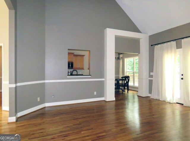 unfurnished living room with high vaulted ceiling, dark wood-type flooring, and a notable chandelier