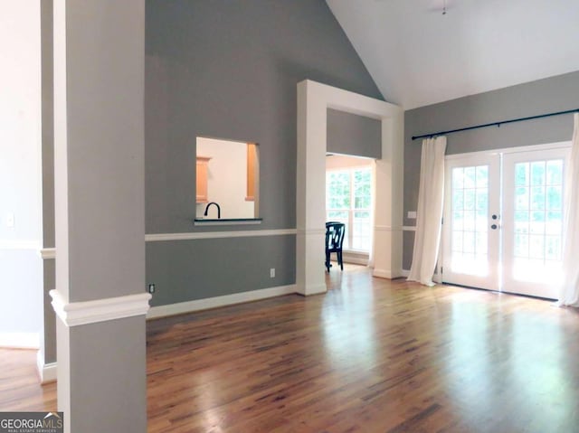 unfurnished living room with ornate columns, wood-type flooring, french doors, and high vaulted ceiling