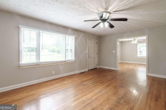 empty room with a textured ceiling, plenty of natural light, ceiling fan, and light wood-type flooring