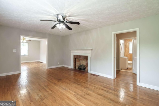 unfurnished living room with a textured ceiling, ceiling fan, a brick fireplace, and hardwood / wood-style flooring