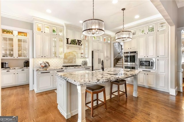 kitchen featuring light wood-type flooring, a chandelier, built in appliances, a kitchen bar, and a kitchen island with sink