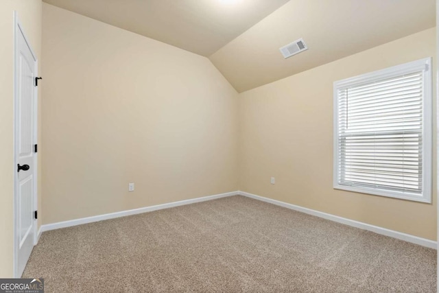 carpeted empty room with visible vents, vaulted ceiling, and baseboards