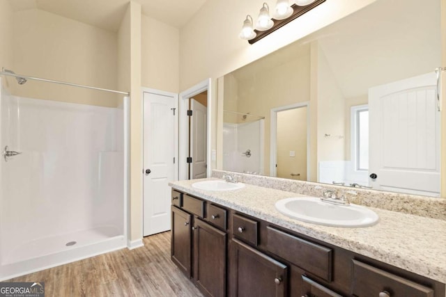 bathroom with double vanity, wood finished floors, a sink, and a shower stall