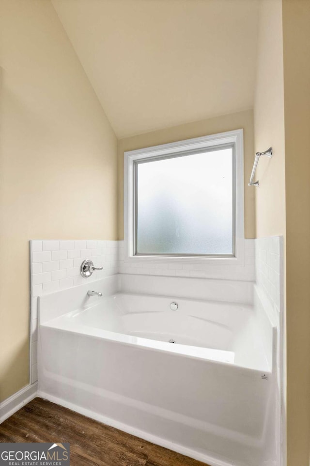 bathroom with lofted ceiling, wood finished floors, and a garden tub