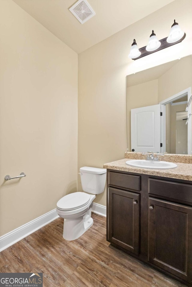 bathroom featuring toilet, wood finished floors, vanity, visible vents, and baseboards