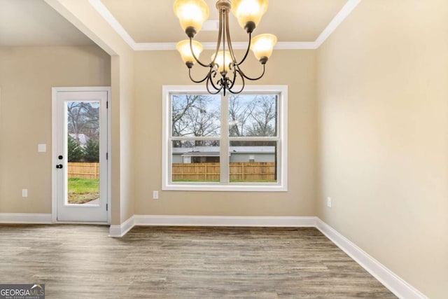 unfurnished dining area with baseboards, crown molding, wood finished floors, and a notable chandelier