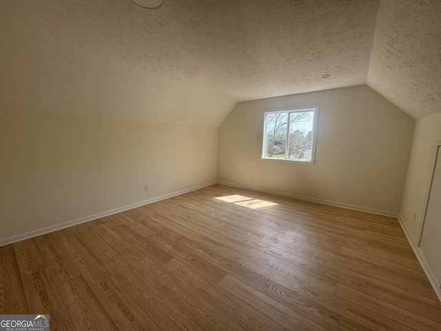 bonus room with light wood-style flooring, baseboards, and a textured ceiling