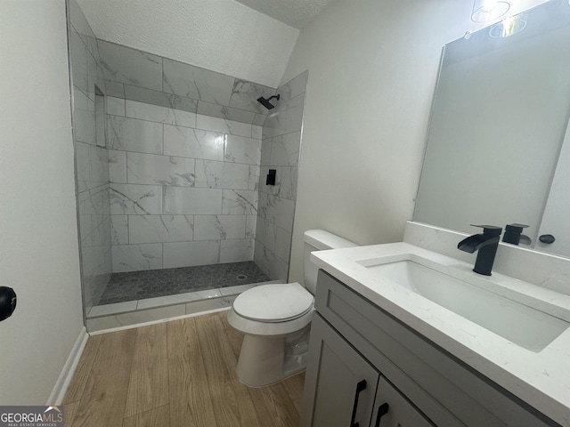 bathroom with toilet, vanity, wood finished floors, and tiled shower