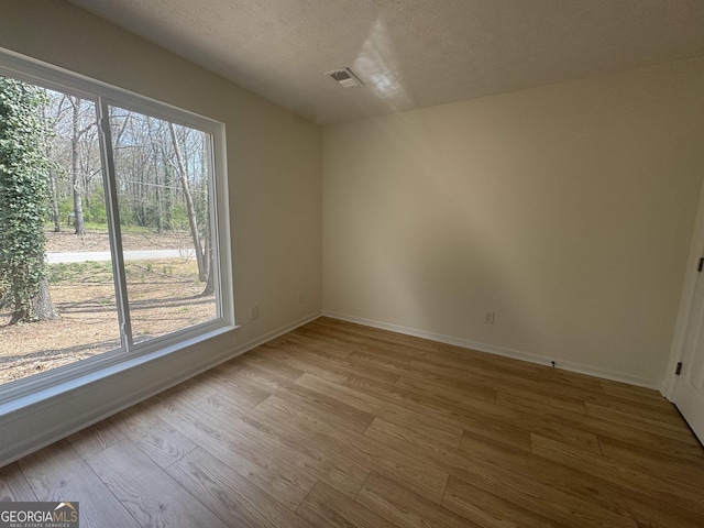 spare room with a textured ceiling, wood finished floors, visible vents, and baseboards