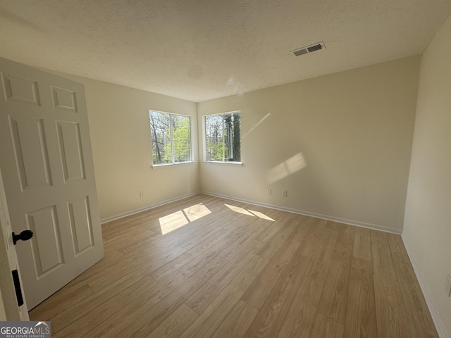 unfurnished room featuring visible vents, light wood-style flooring, and a textured ceiling