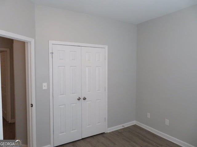 unfurnished bedroom with dark wood-style floors, a closet, and baseboards