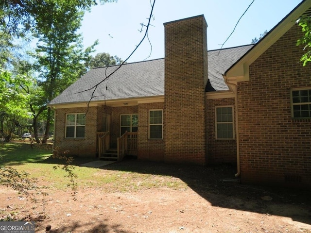 back of house featuring brick siding, roof with shingles, and a chimney