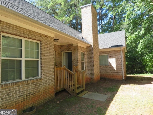 exterior space featuring a shingled roof, brick siding, and a chimney