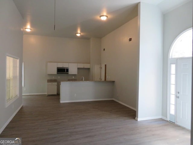 kitchen featuring visible vents, stainless steel microwave, wood finished floors, a high ceiling, and white cabinets