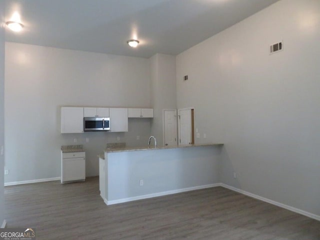 kitchen featuring stainless steel microwave, visible vents, light wood-style flooring, a peninsula, and white cabinets