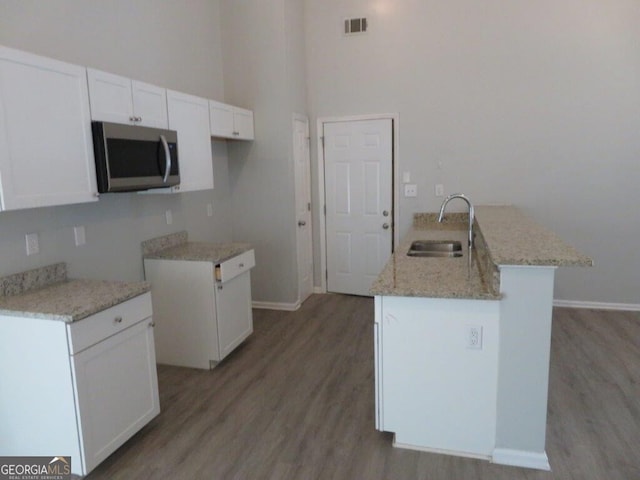 kitchen with a sink, stainless steel microwave, light stone counters, white cabinetry, and a peninsula